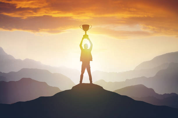 silhouette-of-a-man-holding-a-trophy-at-sunset-picture-id1202740292