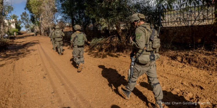 Soldiers in uniform walking along a dirt trail in a rural setting, surrounded by trees and fencing, demonstrating security and patrol activities.
