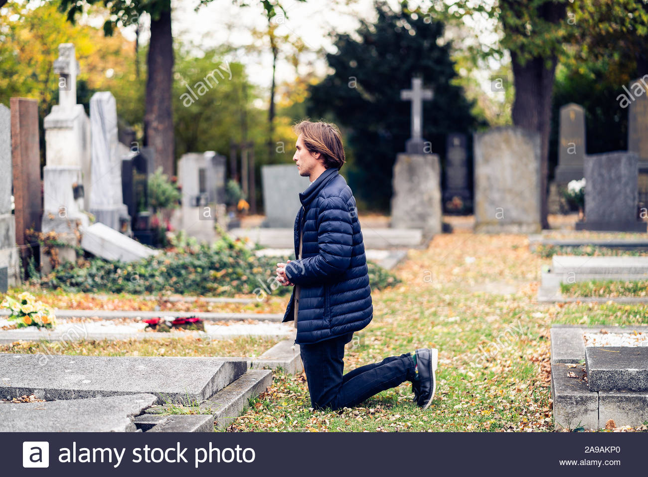 mourning-young-man-kneeling-in-front-of-a-grave-on-a-cemetery-during-a-sad-autumn-day-2A9AKP0.jpg