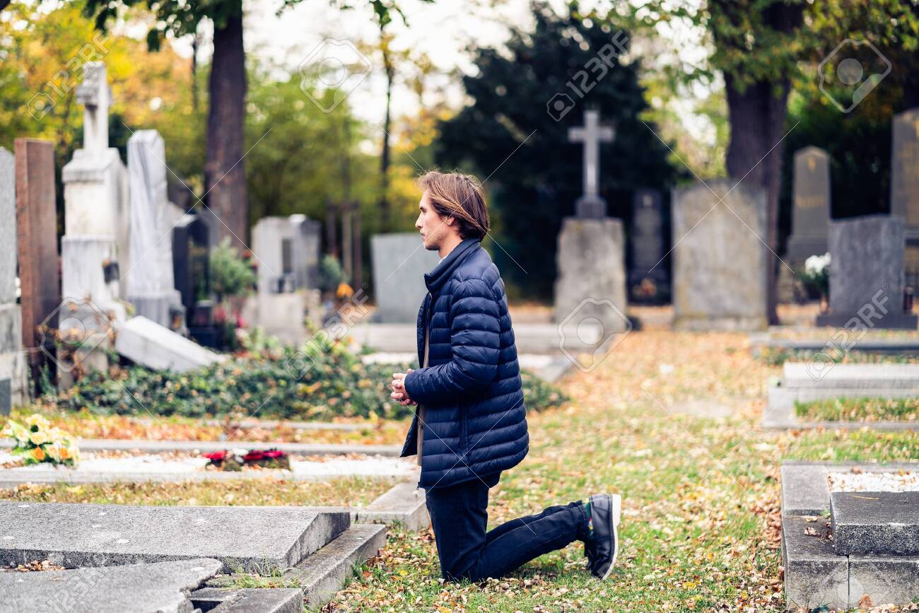 Mourning young man kneeling in front of a grave on a cemetery during a sad autumn day. - 133902856